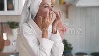 <strong>靠近点</strong>，头上有毛巾的女人在脸上涂抹保湿霜，动作缓慢